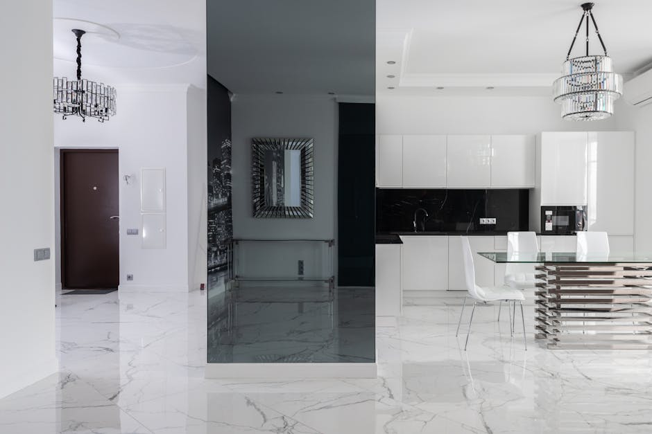 Interior of spacious contemporary house with dining table and chairs under chandelier next to open kitchen with cupboards near hallway