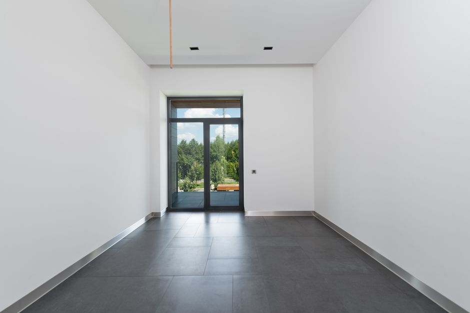 Interior of spacious room with tile flooring and white walls with glass doors in daylight